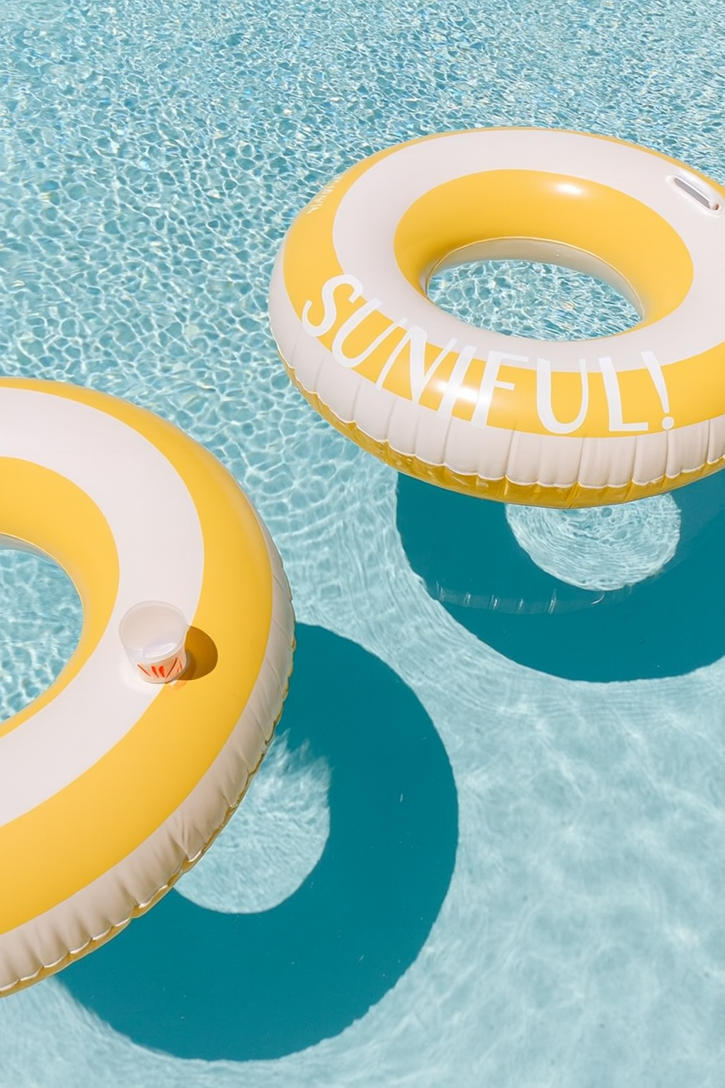 Two inflatable rings with 'SUNNY!' text floating on clear blue water.